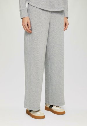 Pantalons larges à côtes grises en tissu doux, dotés d'une coupe décontractée et de poches latérales, associés à des baskets de couleur claire.