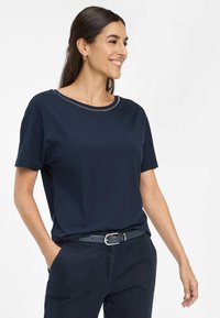 Marineblå kortærmet t-shirt med rund halsudskæring og sølvfarvet syning. Blødt stof, afslappet pasform, parret med mørke bukser og et bælte.