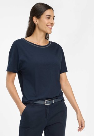 Marineblauw t-shirt met korte mouwen en een ronde halslijn, met zilverkleurige stikdetails. Zachte stof, losse pasvorm, gecombineerd met donkere broek en een riem.