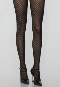 Černé punčochové kalhoty se vzorem diamantové mřížky, v kombinaci s černými lodičkami na vysokém podpatku, které mají řemínky kolem kotníků a špičaté špičky.