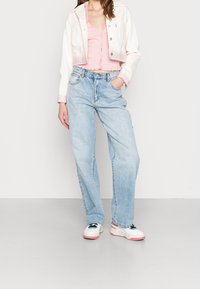 Weiße, verkürzte Jeansjacke mit gestreiften Bündchen, hellrosa gerippter Tanktop, lockere hellblaue Jeans und klobige weiße Sneakers mit Farbakzenten.