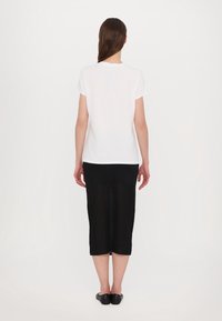 Bílý krátký rukávový triko spárované s černou pletenou midi sukní. Sukně má texturovaný, žebrovaný vzor a je po lýtka.