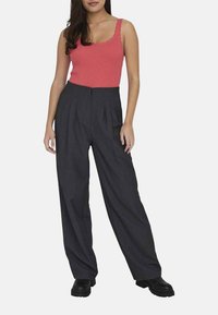 Débardeur en corail à motifs côtelés associé à un pantalon large taille haute en charbon. Le pantalon présente des plis et est porté avec des bottes à plateforme noires.