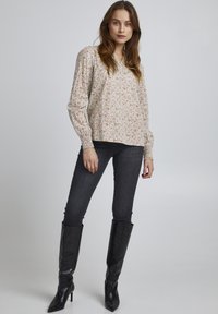 Blomstret langærmet bluse i lys creme med pink- og grønne mønstre, afslappet pasform og smockede håndledsmanchetter. Sammen med mørke skinny jeans og sorte knæhøje støvler.