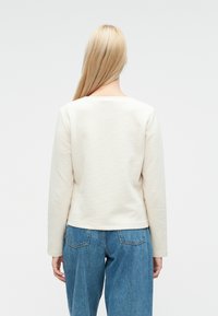 Langärmliges Shirt in Creme mit Rundhalsausschnitt, kombiniert mit locker sitzenden hellblauen Jeans. Schlichtes Design ohne sichtbare Beschläge.