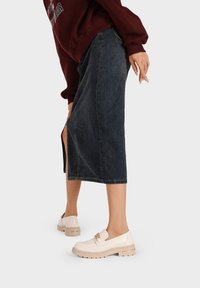 Scarpe slip-on bianche con suola spessa beige, abbinate a una gonna midi in denim scuro con uno spacco laterale. Indossato con un maglione borgogna.