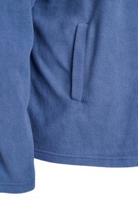 Fleece-takki vaaleansinisellä värillä, pehmeällä tekstuurilla. Sisältää sivutaskun ja suorat saumat helman ja hihojen kohdalla.