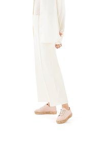 Sneakers leggeri e morbidi di colore rosa chiaro, realizzati in suede, con suola in juta e lacci dorati. Abbinati a pantaloni bianchi a gamba larga e a una maglietta coordinata.