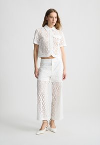 Outfit bianco in pizzo con una maglietta corta a maniche corte e pantaloni ampi, entrambi con motivi a ritagli circolari. Tessuto liscio.