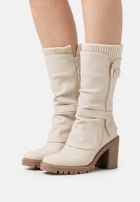 Botas de caña alta de imitación de cuero beige con un diseño holgado, puño de punto acanalado, cremallera lateral y un tacón grueso texturizado.