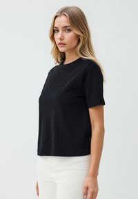 Zwarte korte mouwen t-shirt met ronde hals, gemaakt van gladde stof met een subtiele textuur, gecombineerd met witte broek.