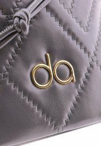 Bolso de cuero gris con un diseño acolchado, con el logotipo dorado "da" y detalles de costura texturizada cerca de la cremallera.