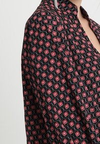 Black blouse featuring a floral pattern in red and white with a stand-up collar. The fabric appears lightweight with a textured finish.