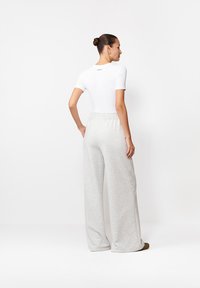 Biała dopasowana koszulka z krótkim rękawem i jasnoszare szerokie spodnie dresowe z elastycznym pasem, przedstawione z tyłu.