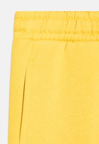 Gelbe Jogginghose mit weicher Textur, elastischem Bund mit Raffung und seitlichen Taschenöffnungen.