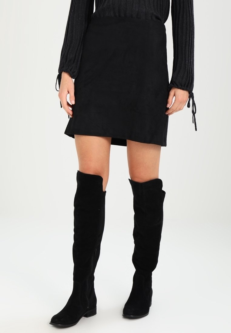 Svart succéskjol med rak skärning, kombinerad med svarta mockastövlar som går över knäna. Outfiten har en texturerad långärmad topp.