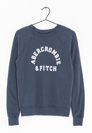 Granatowa bluza z okrągłym dekoltem z białym, zaokrąglonym napisem "ABERCROMBIE & FITCH" na piersi, wisząca na czarnym metalowym wieszaku.