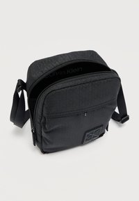 Μαύρη τσάντα χιαστί με υφή καπιτονέ, διαμερίσματα με φερμουάρ, ρυθμιζόμενο λουρί και λογότυπο Calvin Klein στο μπροστινό μέρος.