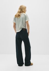 Ljust grå t-shirt med kort ärm och uppvikta ärmar, i kombination med mörkblå vida jeans. Märkbar brun läderlapp på midjan.