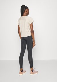 Beige kortärmad topp med en kontrasterande rygg, kombinerad med figurnära svarta leggings och ljusrosa sneakers. Slät tyg med minimala detaljer.