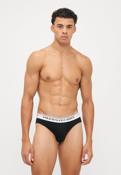 Schwarze Brief-Unterwäsche mit einem weißen "POLO RALPH LAUREN"-Bund, weichem Stoff und figurnaher Passform. Modell zeigt die Vorderansicht.