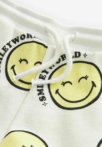 Białe bawełniane szorty z żółtymi wzorami uśmiechniętej buzi i czarnym napisem "SMILEYWORLD", z prążkowanym pasem w talii i sznurkiem.