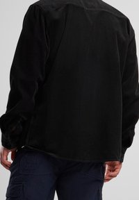 Chemise en velours côtelé noir à manches longues, dotée d'une surface texturée côtelée et de poignets boutonnés. Coupe décontractée avec un ourlet incurvé.