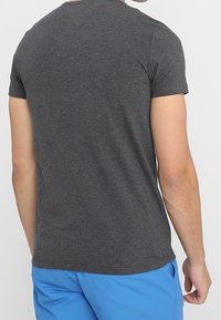 Graues T-Shirt mit kurzen Ärmeln und rundem Ausschnitt. Der Stoff wirkt weich und glatt, passt eng am Oberkörper an, ohne sichtbare Details.