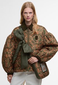 Puffowana zielona kurtka z miedzianymi haftami kwiatowymi, wyrazistym kołnierzem i dużymi rękawami. W zestawie znajduje się zielona kokarda i torebka.