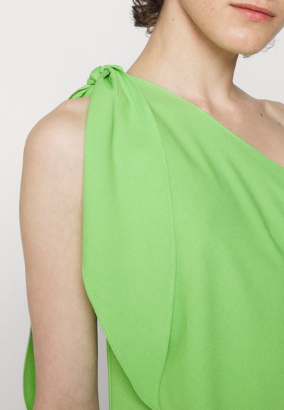Πράσινη ασύμμετρη μπλούζα από απαλό ύφασμα, με λεπτομέρεια κόμπου στον ώμο και ρέουσα γαζί, με διακριτές ραφές.