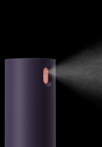 Dispositivo spray cilindrico viola con un pulsante rosa e una nebbiolina fine che esce dalla parte superiore, su sfondo nero.