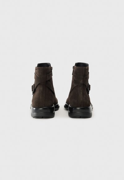 Bottes chelsea en daim marron avec un bord en cuir lisse, fermeture éclair et semelles en caoutchouc ; comportent des sangles à boucle sur les côtés.