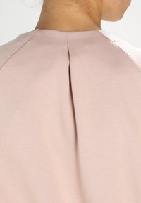 Felpa rosa chiaro con collo rotondo, dotata di una piega sul retro e maniche raglan. Tessuto morbido, superficie liscia, dettagli di design minimali.