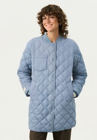 Quilttet blå puffjakke med rund hals, knaplukning og en lomme. Har et struktureret diamantmønster og ribbede manchetter.