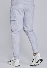 Sive hlače s tapered dizajnom, cargo žepi in rebrastimi manšeti, v kombinaciji z belimi športnimi čevlji z črnimi detajli.