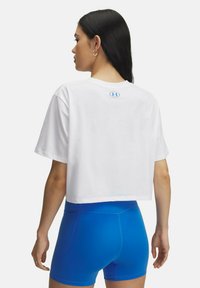 White cropped t-shirt with short sleeves, featuring a blue logo at the back. Worn with bright blue fitted shorts. Smooth cotton texture.