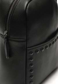 Černý kožený batoh s texturovaným povrchem, který má zipové uzavření a boční kapsu zdobenou černými hroty.