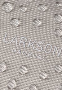 Közelkép egy texturált szövet felületéről, amelyen vízcseppek láthatók, és a "LARKSON HAMBURG" szó világos betűkkel nyomtatva.