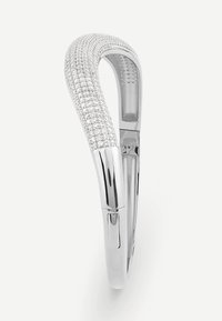 Srebrna bransoletka o zakrzywionym kształcie, ozdobiona małymi przejrzystymi kamieniami szlachetnymi, z polerowanym wykończeniem. Posiada zapięcie zapewniające bezpieczne noszenie.