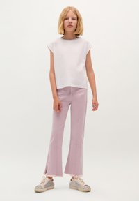 White, short-sleeve top paired with pink flared jeans featuring a raw hem, complemented by silver-accented sneakers. Simple and casual design.