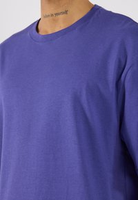 Violet kokvilnas t-krekls ar apaļu kakla izgriezumu. Īsas piedurknes un gluda tekstūra. Redzami nav raksti vai metāla elementu. Vienkāršs dizains bez rotājumiem.