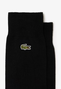 Calze nere con una texture a costine, caratterizzate da un piccolo logo di coccodrillo ricamato in verde sul lato.