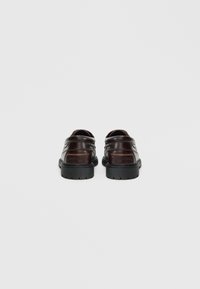 Σκούρα καφέ δερμάτινα παπούτσια με υφή και υπερυψωμένες ραφές, με παχιά μαύρη ελαστική σόλα και στρογγυλεμένη πίσω πλευρά.