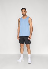 Ανοιχτό μπλε αμάνικο αθλητικό τοπ συνδυασμένο με μαύρο σορτς, λευκές κάλτσες Nike και λευκά αθλητικά παπούτσια, με λογότυπα Nike στα ρούχα.