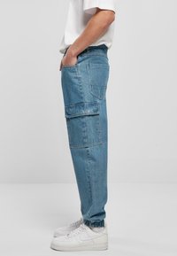 Lysblå denim cargo bukser med en afslappet pasform, der har to sidelommer og elastik ved anklerne. Båret med hvide sneakers.