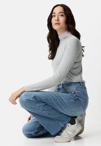 Grijze coltrui, blauwe jeans met wijde pijpen en witte sneakers. Soepele stoftexturen en een casual pasvorm met grote broekspijpen.