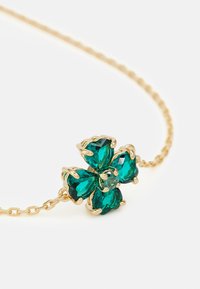 Collar de cadena de oro con un colgante floral que presenta cuatro piedras en forma de corazón de color verde esmeralda y una piedra central redonda.