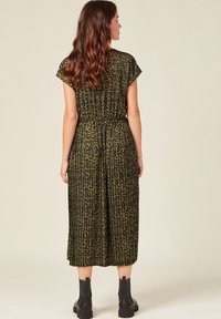 Vestido hasta la rodilla, de color verde olivo con estampado de leopardo negro, mangas cortas, tejido plisado, cintura elástica y botas negras hasta el tobillo.