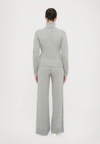 Grauer gestrickter Rollkragenpullover mit gerippten Akzenten, kombiniert mit weit geschnittenen grauen Strickhosen. Weiche Textur, taillierte Passform, insgesamt lockere Silhouette.