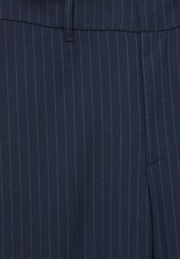 Tissu bleu marine avec de fines rayures verticales bleu clair, montrant une partie de la ceinture et la couture de la poche d'un pantalon sur mesure.